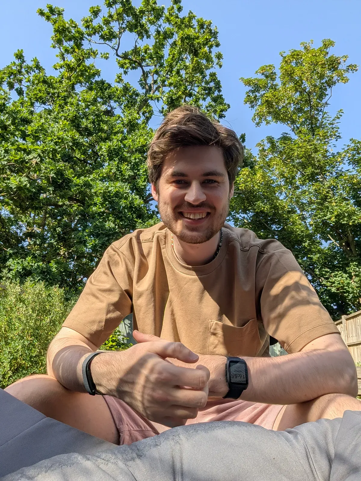 A photo of Jonothan sitting outdoors on a sunny day wearing a Pebble Time 2 on one wrist and a Fitbit on the other